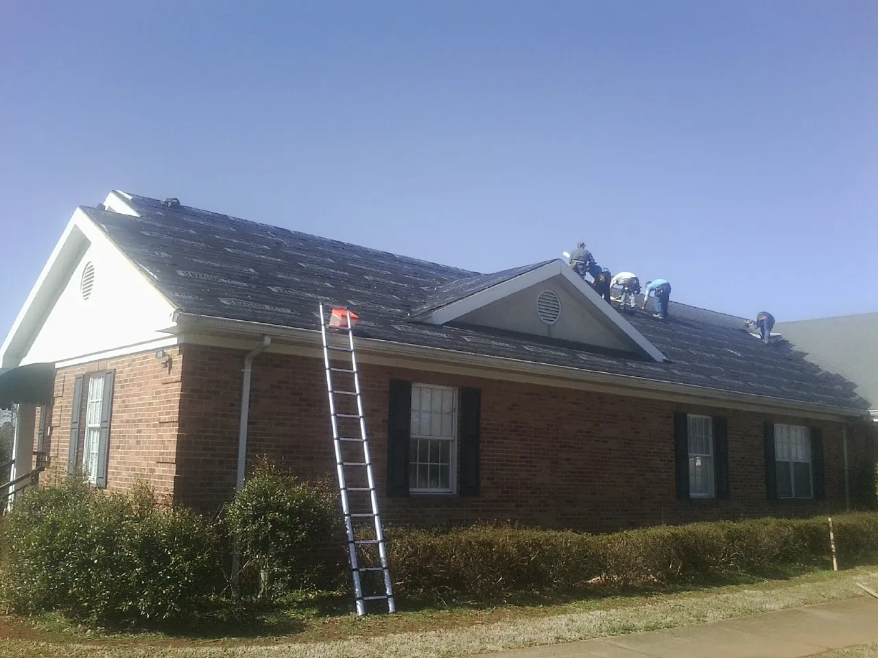 Crew tearing shingles off a brick ranch roof with a ladder set — Emergency Roof Repair work by our crew in Trexlertown