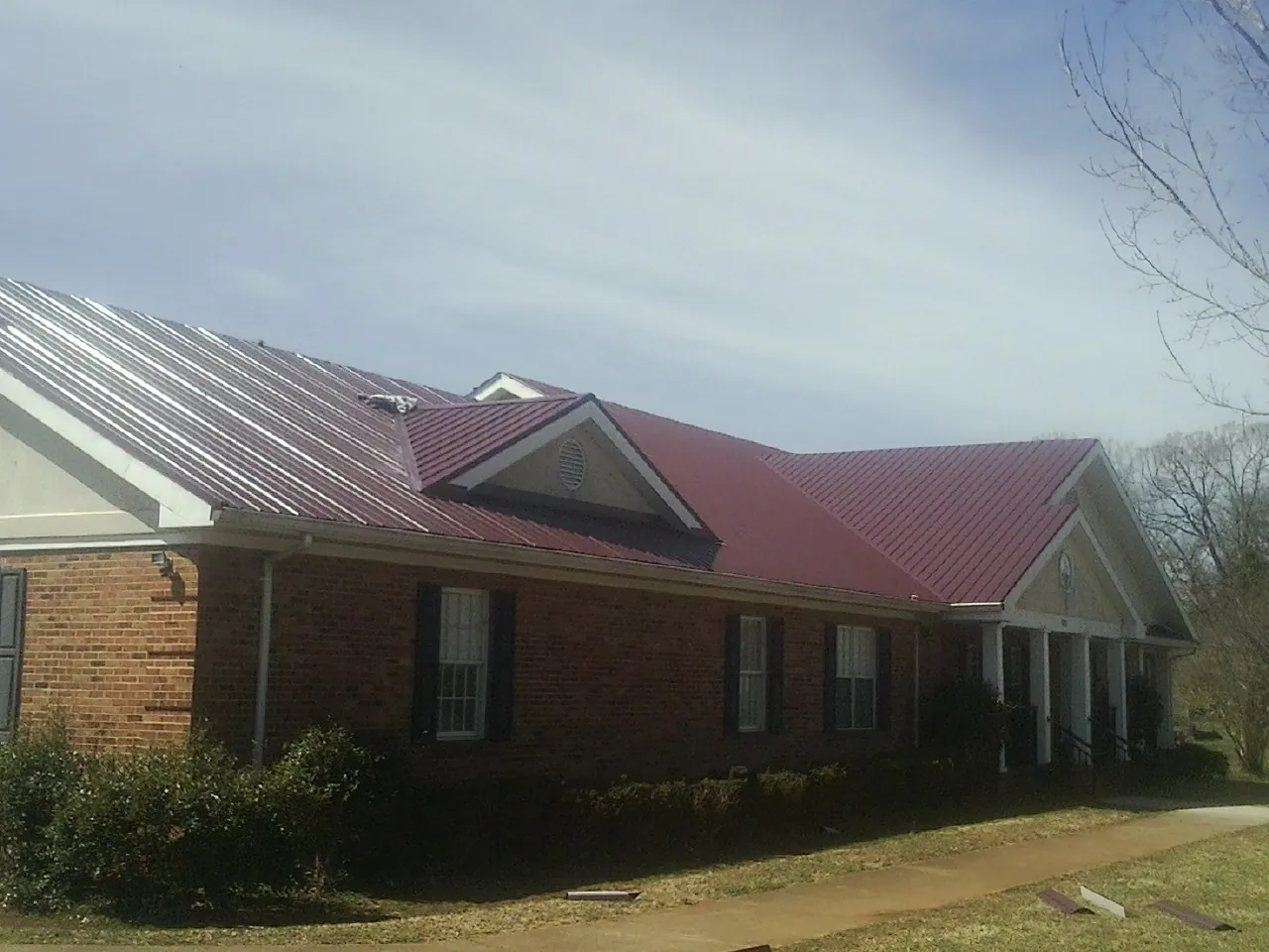 Red metal roof with gabled entries on a long brick building, from a Hail Damage Roof Repair job in Trexlertown