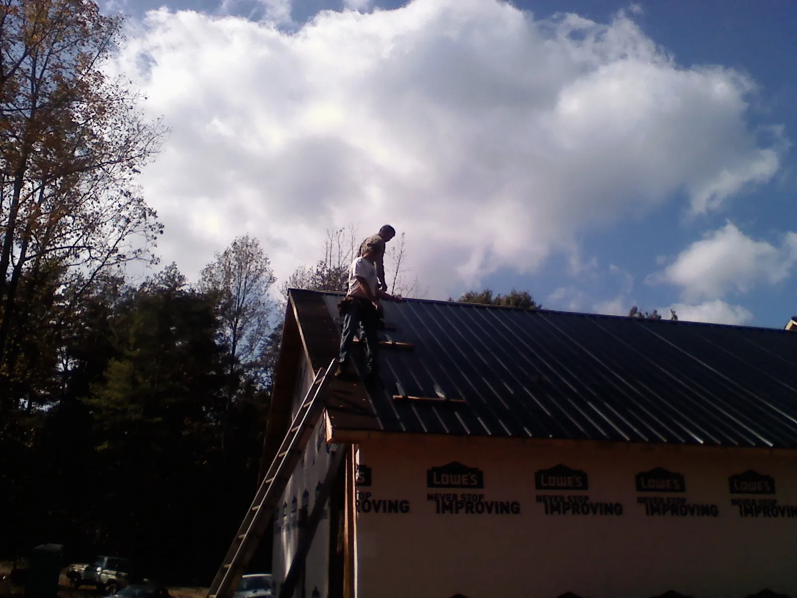 Roofer fastening dark metal panels high against a cloudy sky, from a Roof Inspection job in Trexlertown
