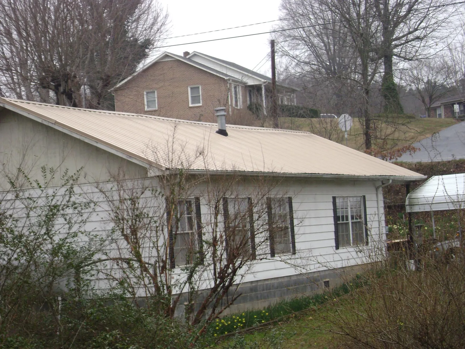 Tan metal roof on a white sided house set into a hillside — Commercial Roofing by Roofing Brothers in Trexlertown
